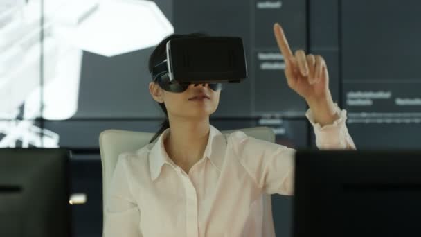 4K Engineer wearing virtual reality viewer at her desk with animated graphic of architectural structure in background - Filmati, video