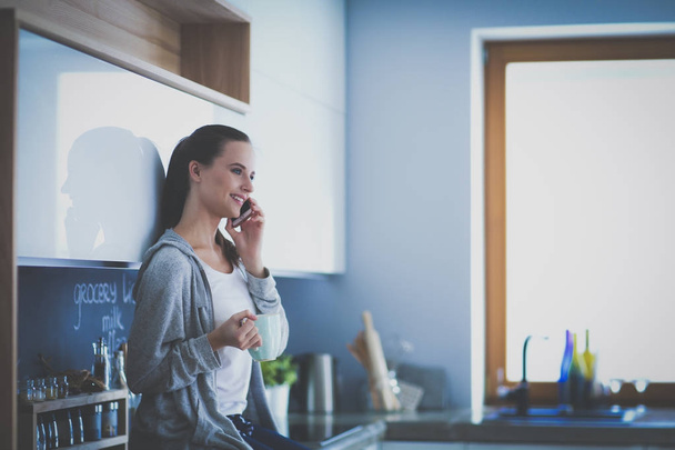 Woman using mobile phone sitting in modern kitchen. - Photo, image