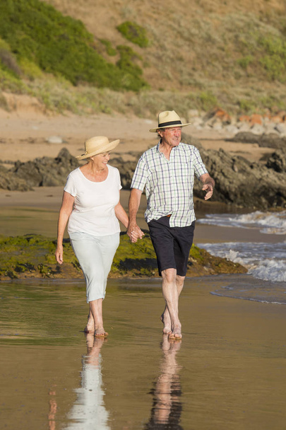 reizendes älteres Ehepaar in den 60ern oder 70ern im Ruhestand, das glücklich und entspannt am Strand am Meer spaziert und romantisch zusammen altert  - Foto, Bild
