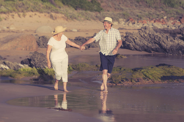 lovely senior mature couple on their 60s or 70s retired walking happy and relaxed on beach sea shore in romantic aging together  - Photo, image