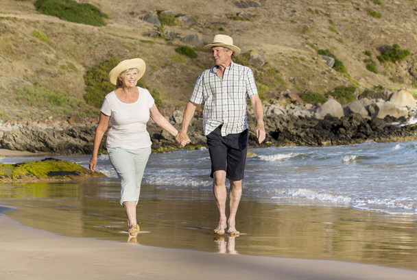 lovely senior mature couple on their 60s or 70s retired walking happy and relaxed on beach sea shore in romantic aging together  - Photo, Image