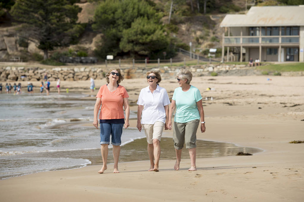 группа из трех пожилых зрелых женщин в возрасте 60 лет, веселящихся вместе, счастливо гуляющих по пляжу, улыбающихся игриво
 - Фото, изображение