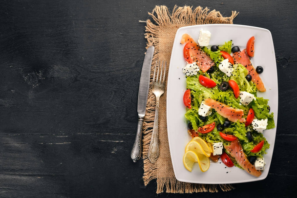 Salmon salad, feta cheese, salad leaves and fresh vegetables on the plate. On a wooden background. Top view. Free space for text. - Foto, Imagen