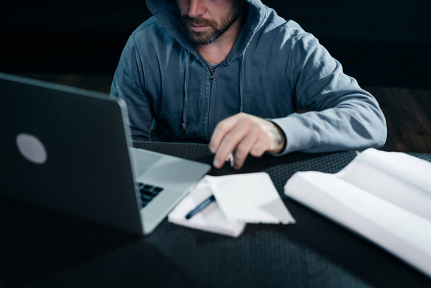 un misterioso hombre barbudo extraño en una capucha se dedica a algo ilegal en una computadora portátil
 - Foto, imagen