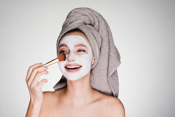 beautiful smiling girl puts a white nutritious mask on her face, on her head a towel - Foto, Imagem