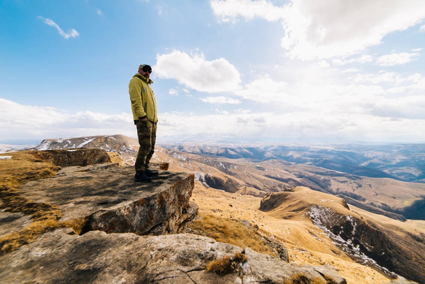 male traveler standing on the edge of the cliff against the background of the Caucasian mountains and blue sky - Photo, Image