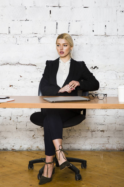 Young blond beauty businesswoman sitting at a office table with laptop, notebook and glasses in suit. Business concept. - Фото, зображення