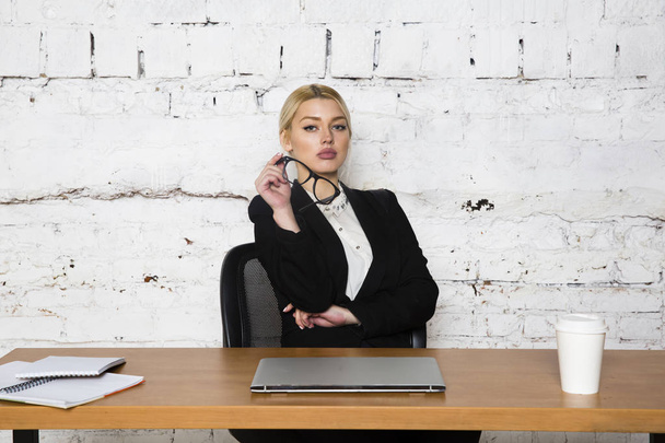 Young blond beauty businesswoman sitting at a office table with laptop, notebook and glasses in suit. Business concept. - Zdjęcie, obraz