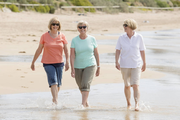 group of three senior mature retired women on their 60s having fun enjoying together happy walking on the beach smiling playful - Photo, Image