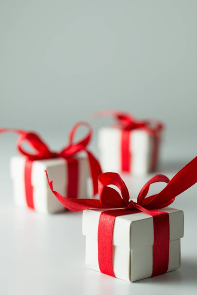 Три білі подарункові коробки з червоною стрічкою в ряд
 - Фото, зображення