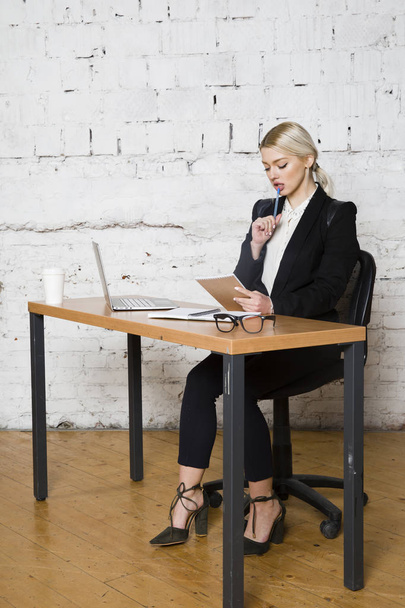 Young blond beauty businesswoman sitting at a office table with laptop, notebook and glasses in suit. Business concept. - Zdjęcie, obraz