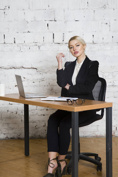Young blond beauty businesswoman sitting at a office table with laptop, notebook and glasses in suit. Business concept. - 写真・画像