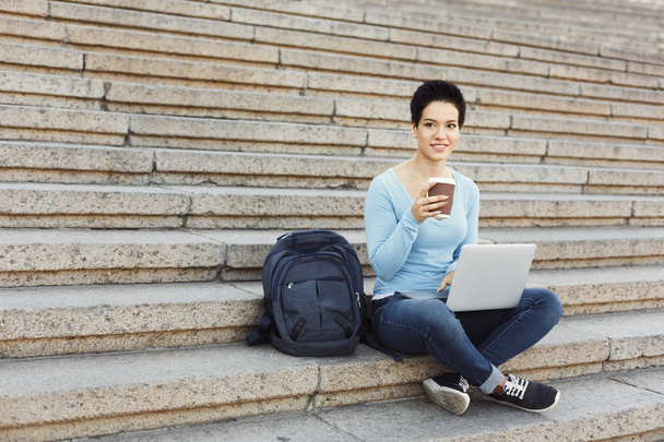 Усміхнена жінка сидить на сходах за допомогою ноутбука
 - Фото, зображення