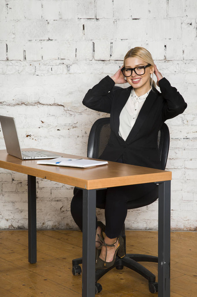 Young blond beauty businesswoman sitting at a office table with laptop, notebook and glasses in suit. Business concept. - Foto, afbeelding