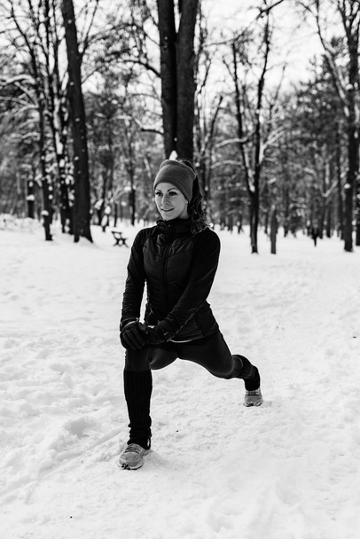 Vrouwelijke atleet uitoefenen in park op winterdag. Muziek luisteren en oefenen - Foto, afbeelding
