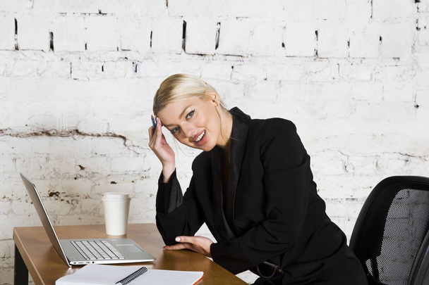 Jovem mulher de negócios de beleza loira sentada em uma mesa de escritório com laptop, notebook e óculos de terno. Conceito de negócio
. - Foto, Imagem