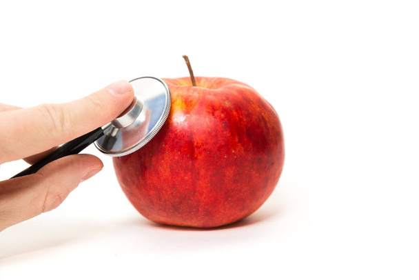 Controle, onderzoek van appels, fruit. Een mens buigt zich over een rode appel met een stethoscoop. Onderzoek van de versheid van de vruchten. Kwaliteitscontrole. Bio groenten. De beste en beproefde appels. Geïsoleerde witte achtergrond. - Foto, afbeelding