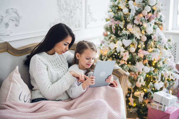 Beautiful young woman and her daughter with the tablet at Christmas time. Close-up. - Photo, Image
