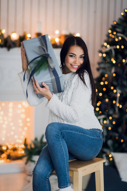 Boldog nő izgatott, hogy nyissa ki a karácsonyi ajándék ül otthon előtt egy karácsonyfa és kandalló - Fotó, kép