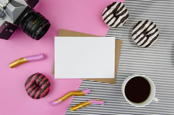 Maquette avec papier blanc propre, café, caméra rétro et beignets, sur fond pastel géométrique rayé rose Pose plate, bureau avec vue sur le dessus
. - Photo, image