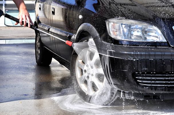 Очистка автомобиля с использованием воды высокого давления. Мужчина моет машину под водой высокого давления в эксплуатации
  - Фото, изображение
