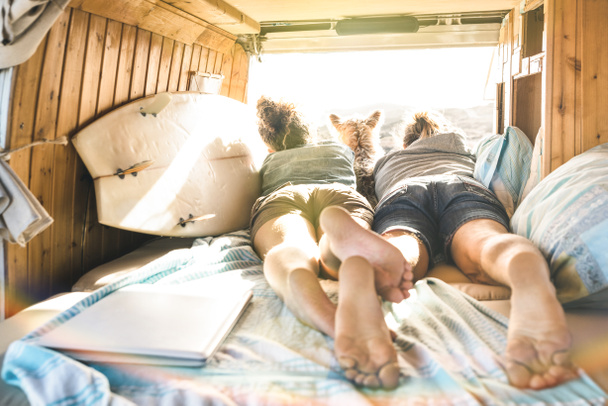 Hipster couple with cute dog traveling together on vintage van transport - Life inspiration concept with hippie people on minivan adventure trip watching sunset in relax moment - Warm sunshine filter - Photo, image