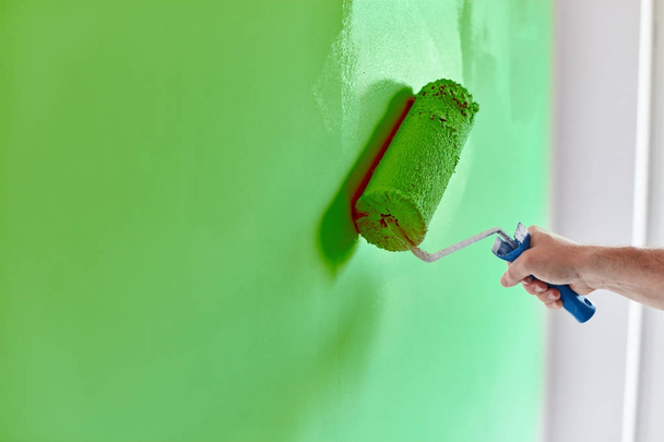 Male hand painting wall with paint roller. Painting apartment, renovating with green color paint - Фото, изображение