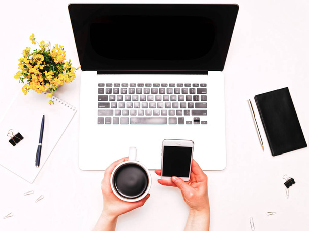 Espaço de trabalho com mão feminina segurando telefone e café flores laptop
 - Foto, Imagem