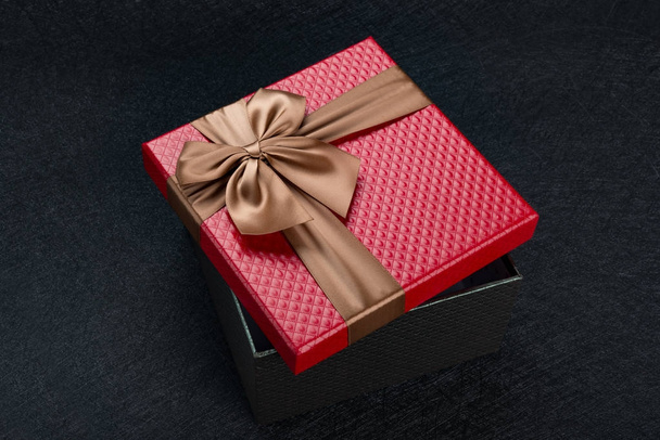 caja de regalo roja con lazo marrón sobre fondo oscuro
 - Foto, imagen