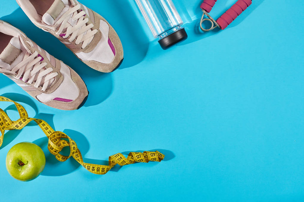 Sneakers with measuring tape on cyan blue background. Centimeter in yellow color near white trainers, close up. - Photo, Image