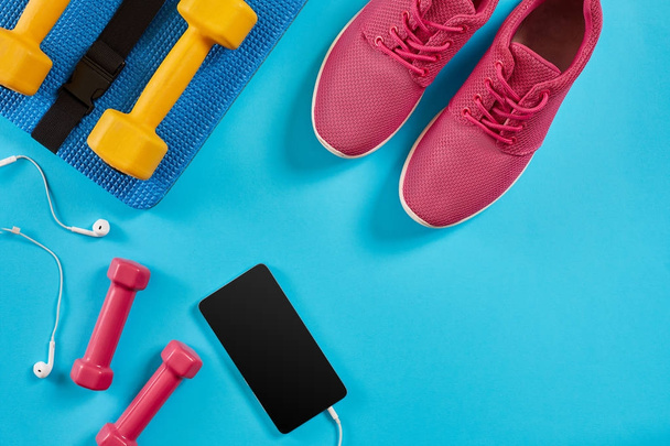 Zapatillas deportivas, mancuernas y teléfono móvil sobre fondo azul. Vista superior. Fitness, deporte y estilo de vida saludable
. - Foto, imagen
