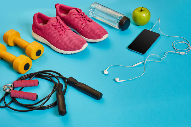 Flat lay of dumbbell, bottle of water, jump rope and sneaker, sport equipments, fitness items, top view - Photo, Image