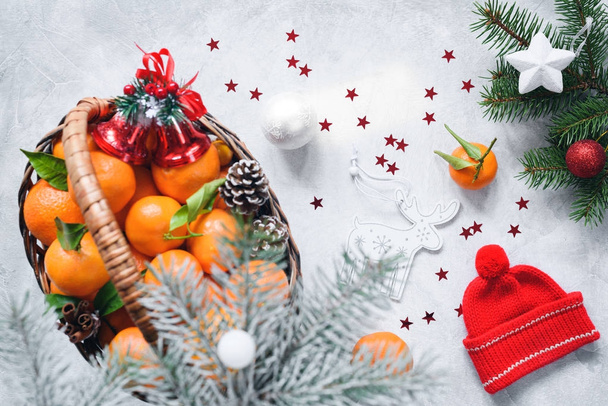 Christmas composition with tangerines in basket, red winter hat, pine cones, fir tree and toys on bright concrete background - 写真・画像