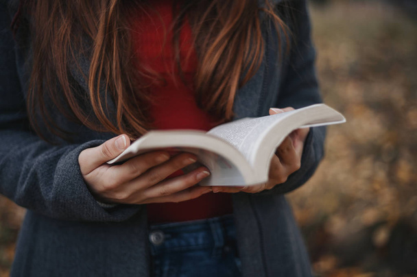 Женщина в теплой одежде держит открытую книгу на открытом воздухе в осеннем парке
 - Фото, изображение
