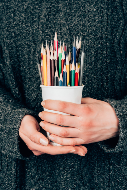 Vue rapprochée des mains féminines tenant une tasse avec des crayons colorés
 - Photo, image