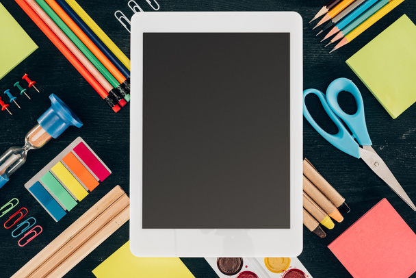 Flachbild-Tablet mit leerem Bildschirm über Hintergrund mit Schulmaterial isoliert auf dunklem Hintergrund - Foto, Bild