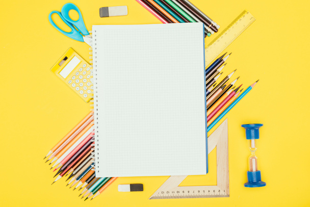 Top view of composition of colorful school supplies with blank notebook isolated on yellow background - Photo, Image