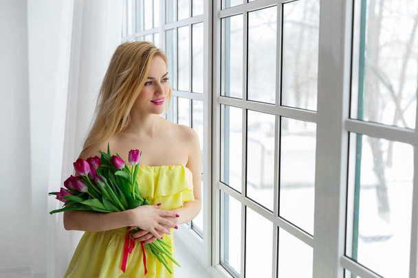 Joven hermosa mujer con manojo de tulipán en vestido amarillo en la ventana
 - Foto, imagen