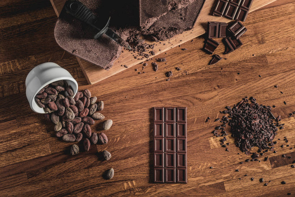 Sweet Table Top View arrangement of Cocoa beans, nibs and Chocolate bars on wooden surface. - Photo, image