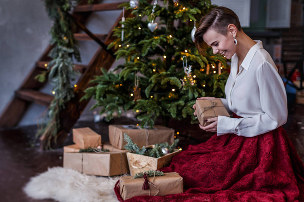Smiling beautiful woman is posing around the Christmas tree with different boxes full of gifts - Foto, Imagem