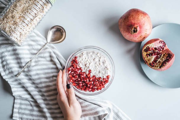 Desayuno saludable - mano femenina con harina de avena con yogur, granada fresca en la mesa
 - Foto, Imagen
