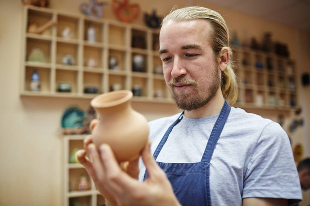 Maestro de la cerámica mirando la jarra nueva en el taller
 - Foto, Imagen