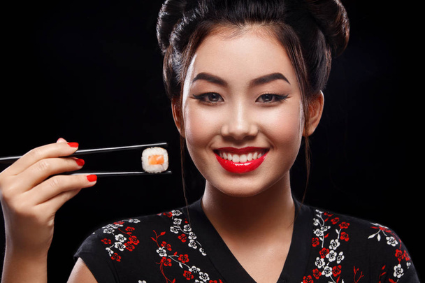 Happy and smiling Asian woman eating sushi and rolls on a black background. - Foto, imagen