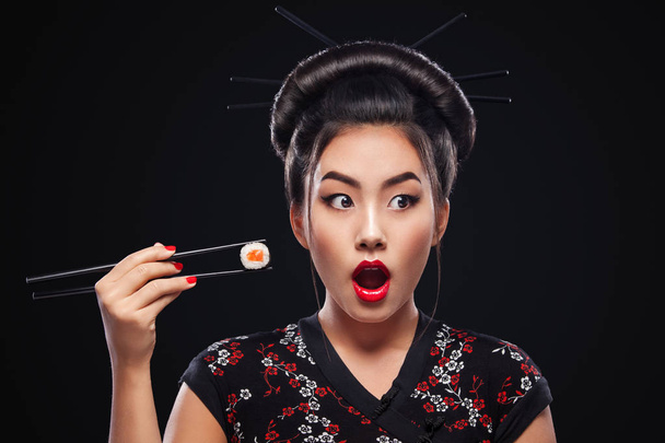 Surprised Asian woman eating sushi and rolls on a black background. - Fotó, kép