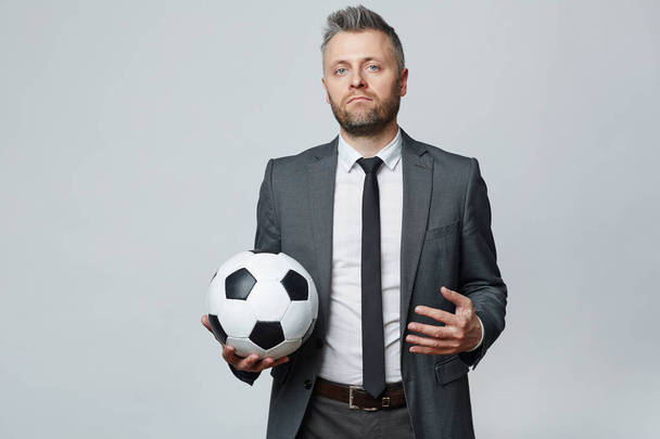 Retrato de estudio de cintura hacia arriba del hombre de mediana edad con pelo gris sosteniendo la pelota de fútbol y mirando a la cámara
 - Foto, Imagen