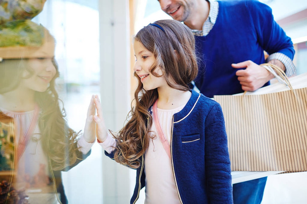 Усміхнена дівчина дивиться на магазин-дисплей на щось цікаве
 - Фото, зображення