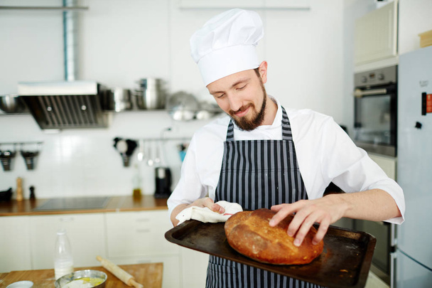 Ζαχαροπλαστικής-φούρναρης αγγίζοντας κακότροπος καρβέλι ψωμί σε δίσκο - Φωτογραφία, εικόνα