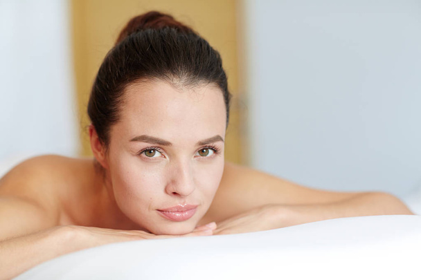Jovem mulher relaxada com maquiagem natural olhando para a câmera no salão de spa
 - Foto, Imagem