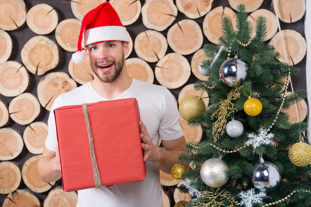 Happy holidays celebration. Santa man with box at xmas tree. xmas and new year presents preparation. Macho in red hat smile with gift. Boxing day concept. - Photo, image