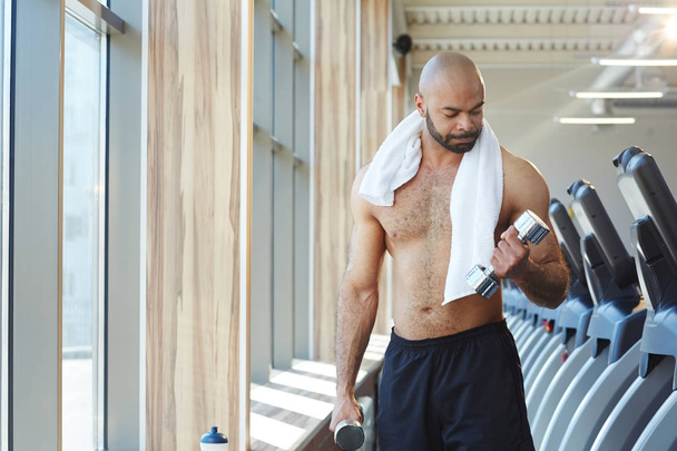 Мускулистый мужчина тренируется с гантелями в тренажерном зале
 - Фото, изображение